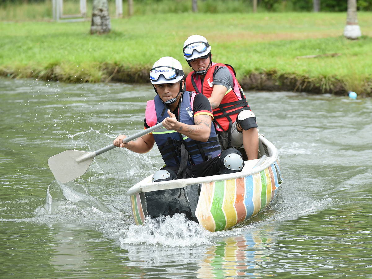 Dos personas con chaleco salvavidas remando una embarcación improvisada en un lago durante una actividad de equipo.