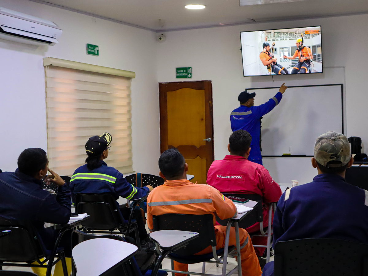 Grupo de trabajadores sentados en un aula siguiendo una presentación proyectada por el instructor.