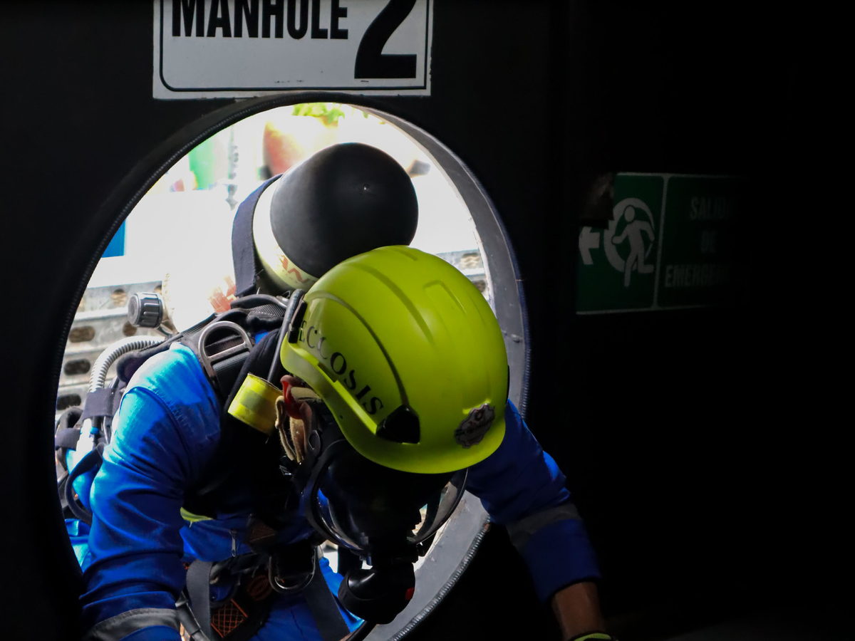Trabajador con equipo de respiración autónoma ingresando por la boca de acceso de un espacio confinado.