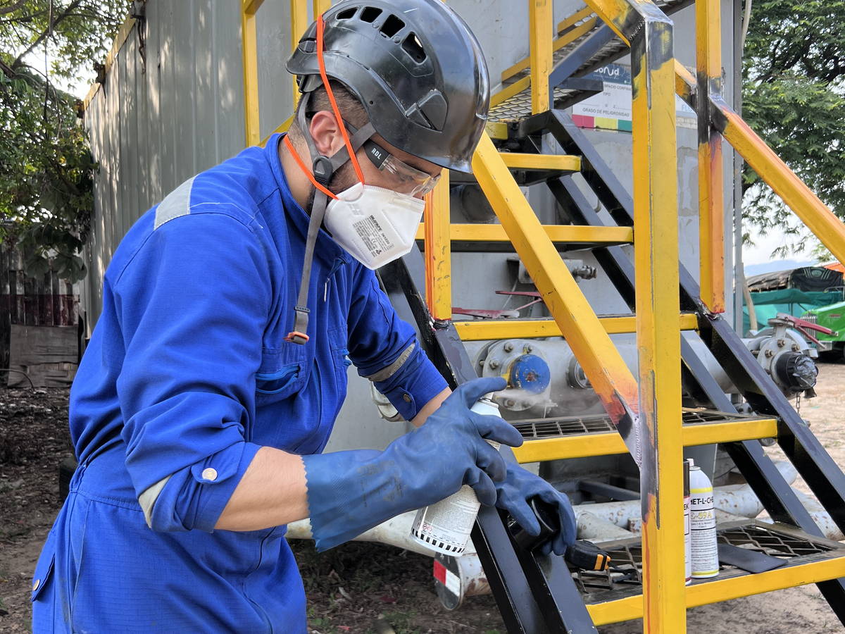 Inspector con mascarilla y guantes revisando la soldadura de una escalera metálica industrial.