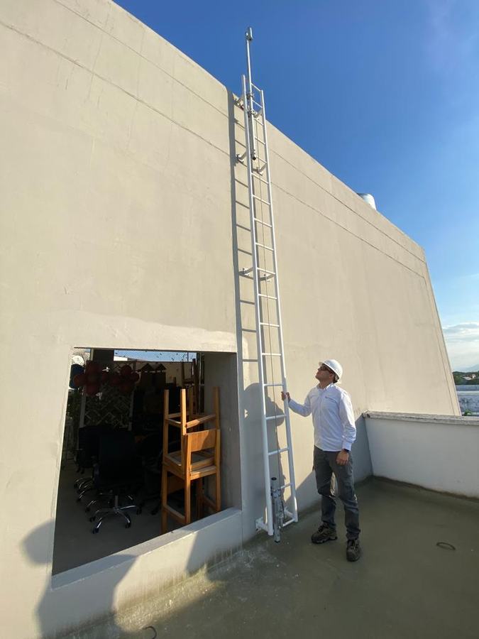 Escalera fija con línea de vida vertical en la fachada de una edificación, con una persona revisando la instalación desde la cubierta.