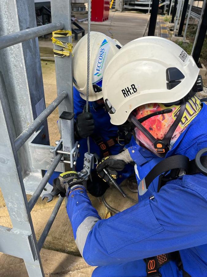 Dos técnicos de Eccosis instalan los componentes de la línea de vida en una escalera metálica.