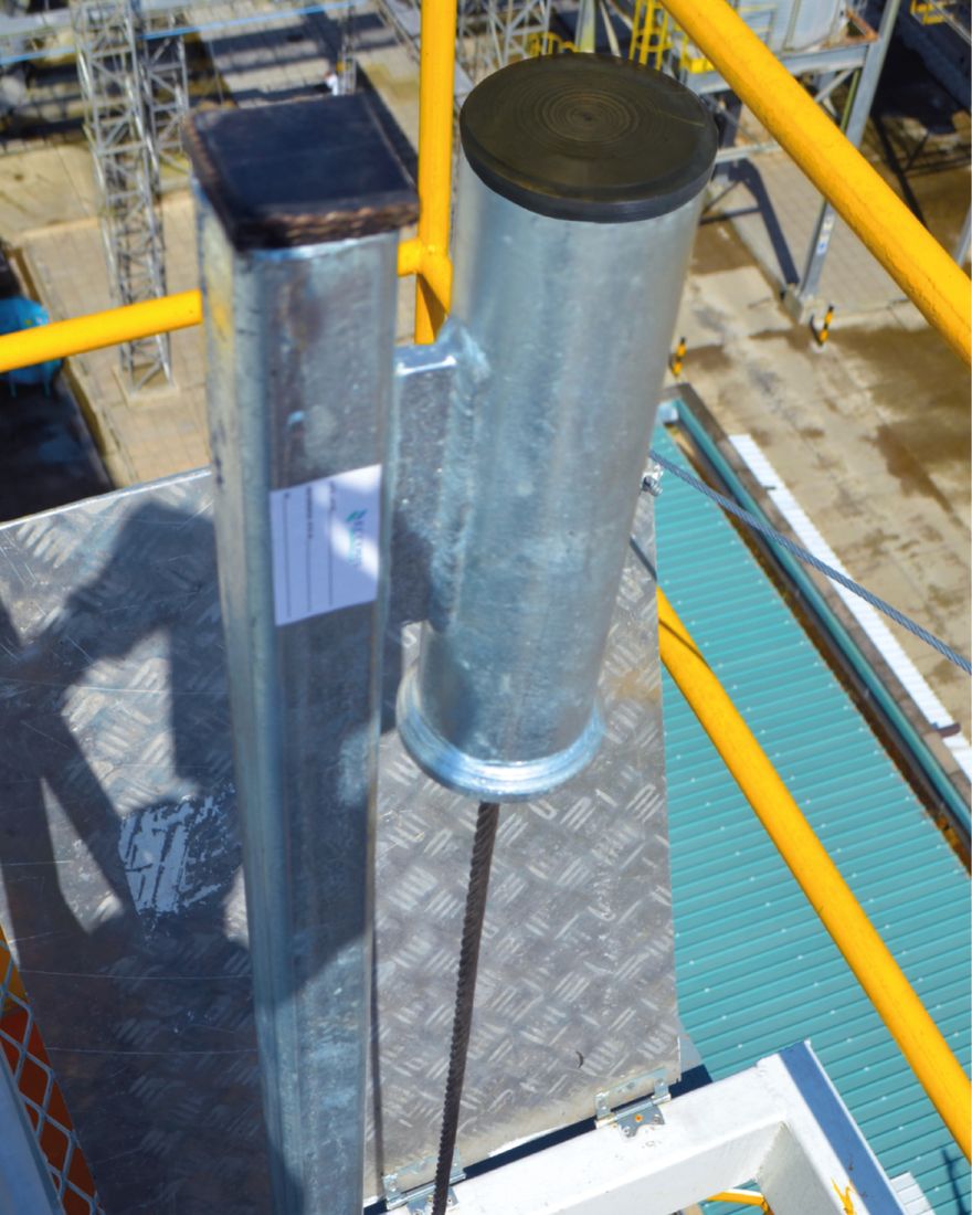 Mástil superior galvanizado de la línea de vida instalado en lo alto de una escalera, con el cable de acero descendiendo.